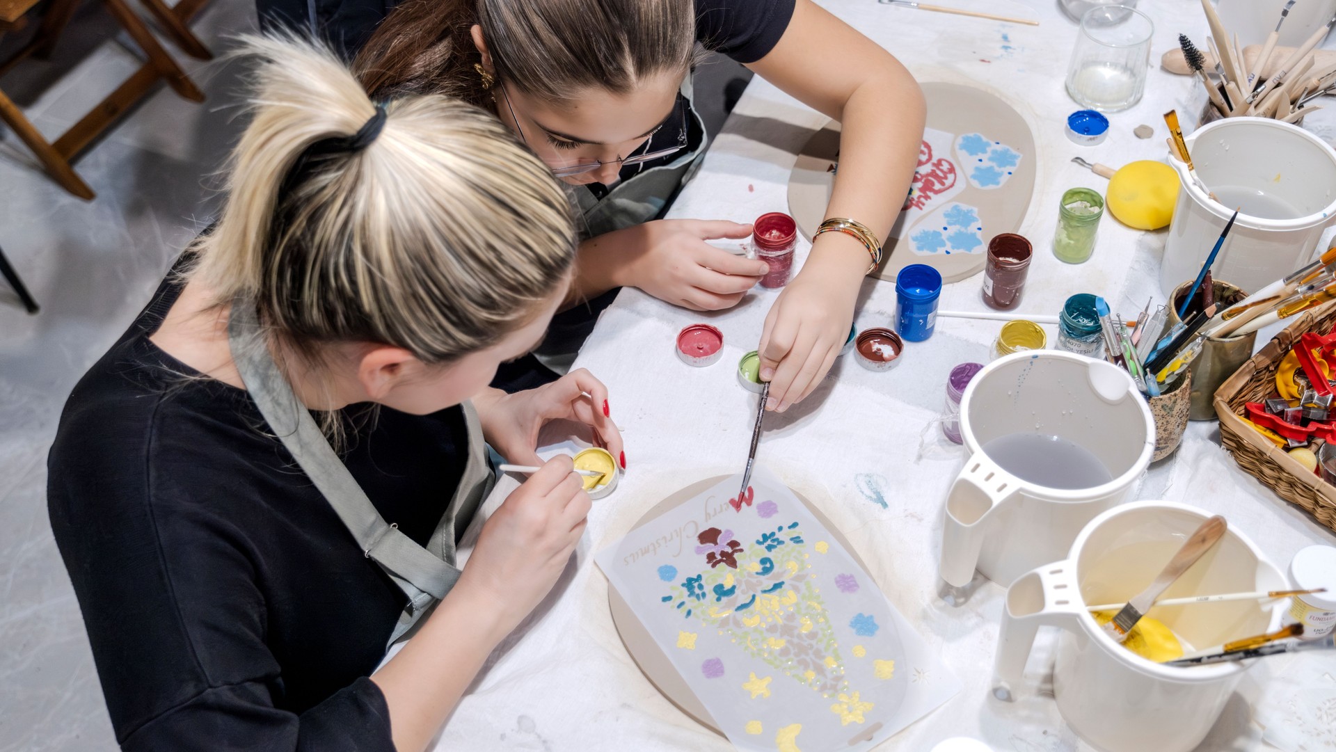 During an art event in a studio, a girl child is painting Christmas ornament shapes she crafted on clay