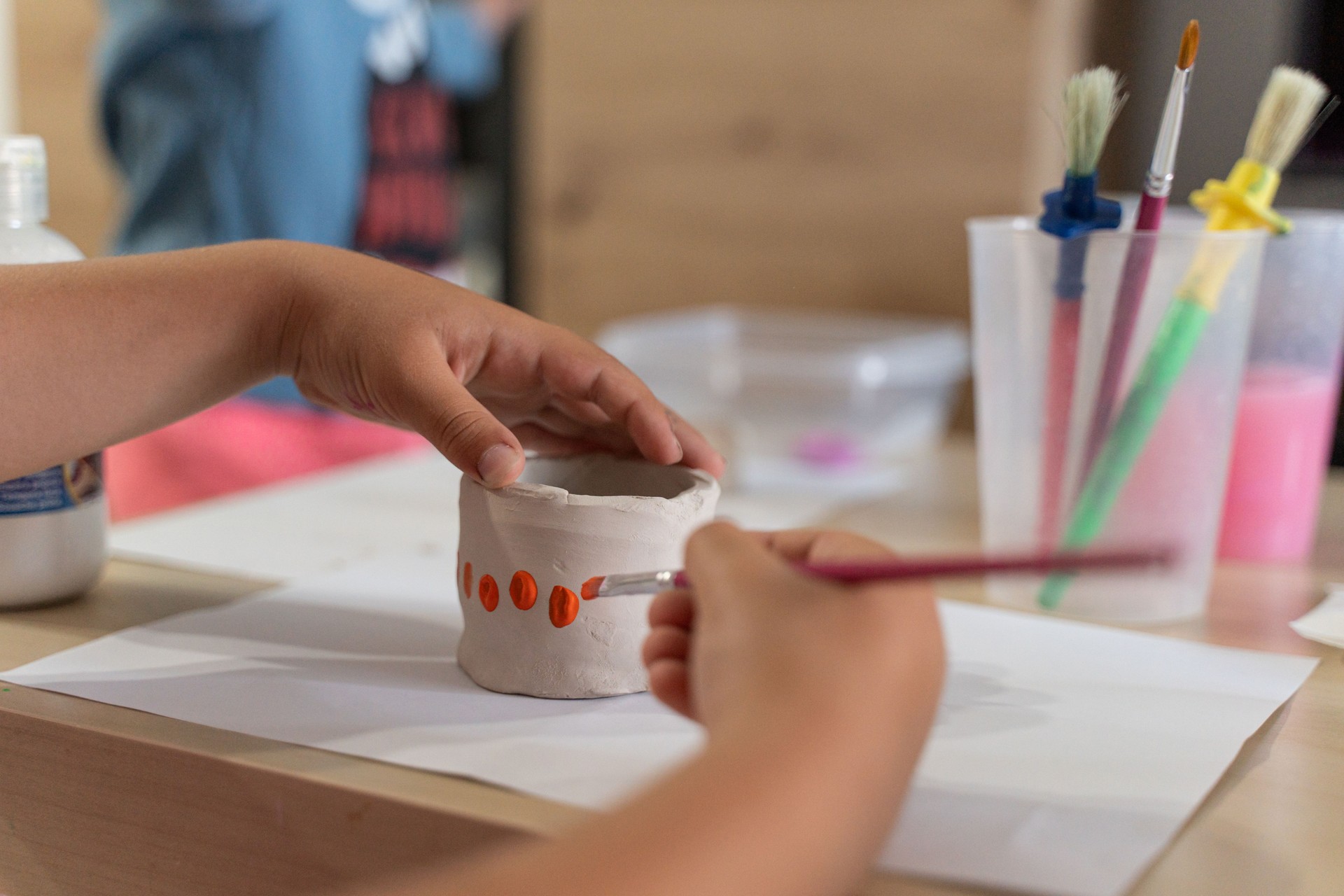 girl painting her clay bowl with a brush