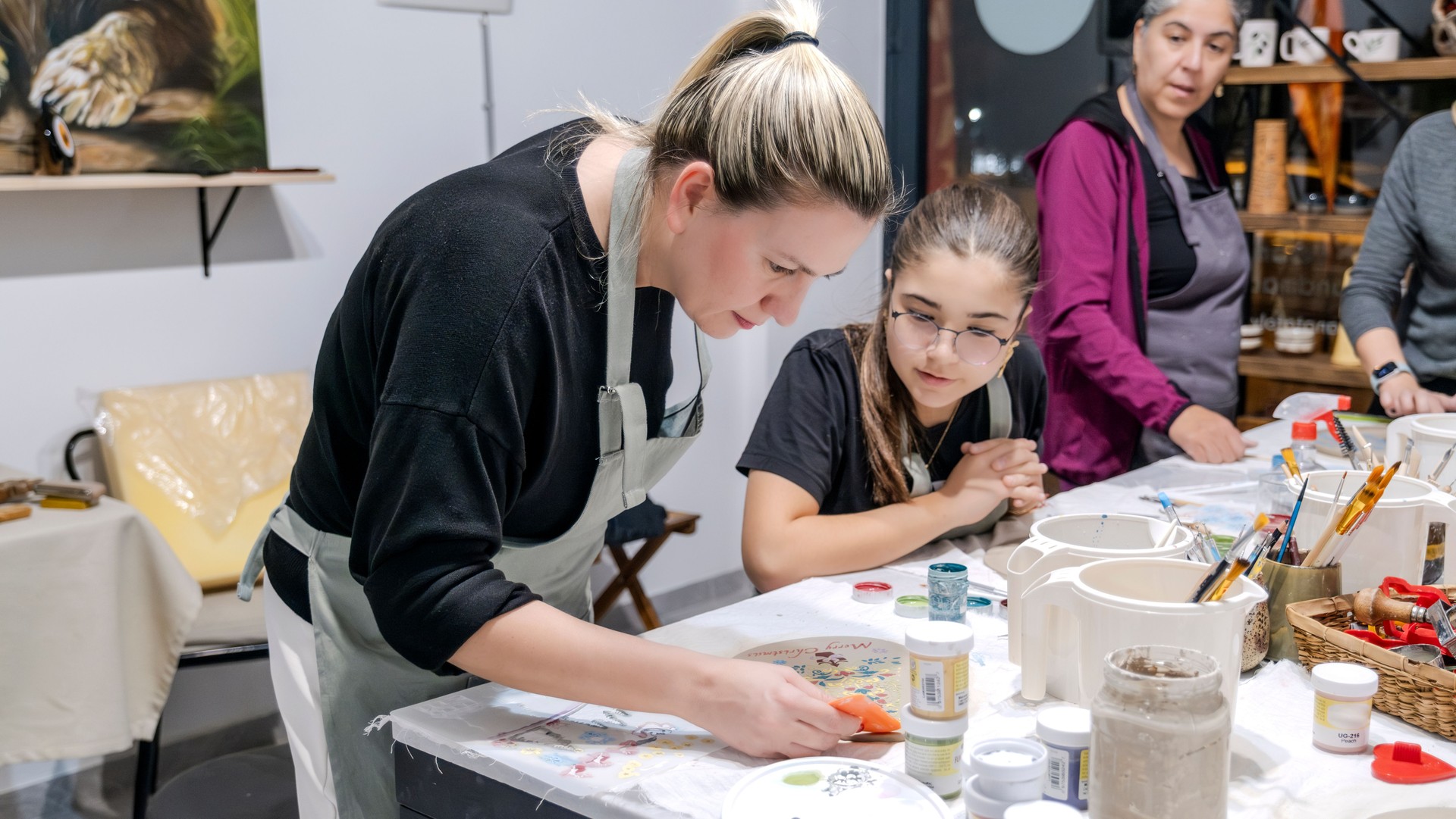 In an art studio during an event, a mother and her young daughter are enjoying quality time together while learning clay shaping as a hobby