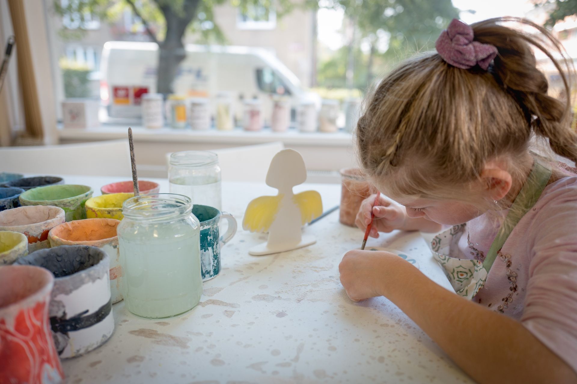 Young girl painting in pottery workshop using colourful paints and brush